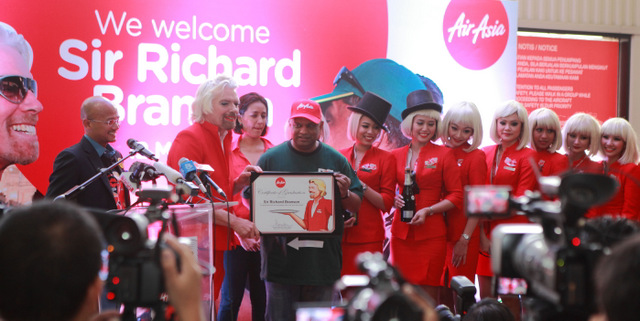 Tony Fernandes presents a flight attendant graduation certificate to Richard Branson