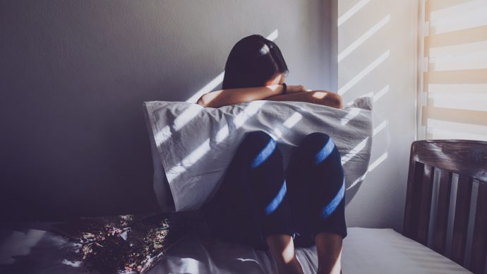 Asian women are sitting hugging their knees in bed. Feeling sad, disappointed in love In the dark bedroom and sunlight from the window through the blinds.Vintage tone. | SUPERADRIANME.com