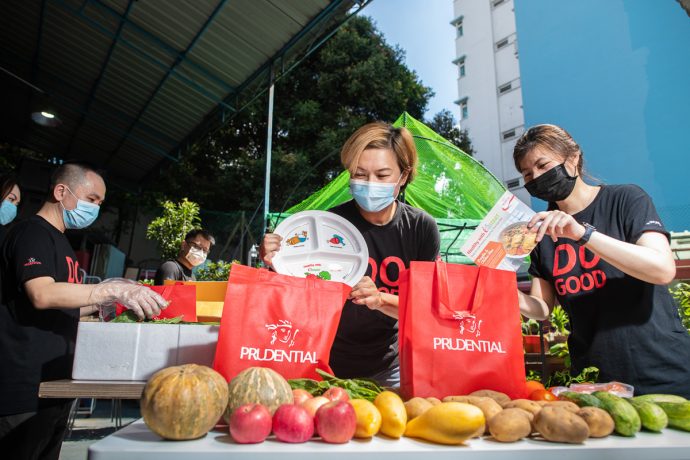 Prudential employee Ms Ariel Ong assembling a care pack consisting of fresh produce, a “Healthy Plate”, and a recipe card, together with her colleagues. 